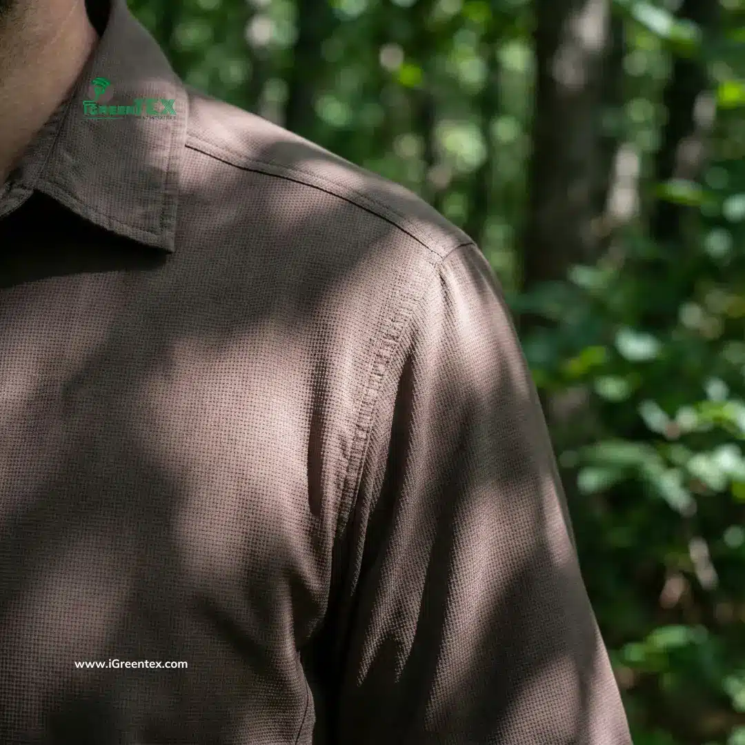 Close-up of a durable brown coffee fabric hiking shirt with sunlight filtering through leaves, highlighting the UV protection and breathability of the sustainable textile in a forest setting.