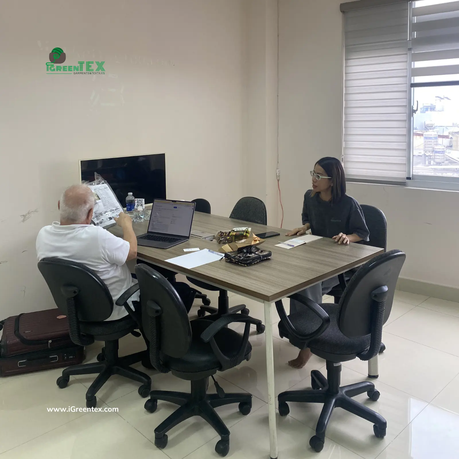 A professional meeting at iGreen Tex Vietnam office where our team is discussing a detailed technical package (tech-pack) with Australian clients. They are reviewing garment construction charts and fabric swatches, proving why iGreen Tex is among the top clothing manufacturers in vietnam for australian brands for high-precision orders.