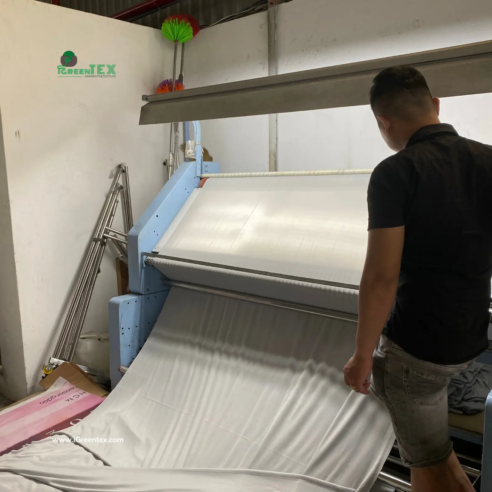 A quality control inspector at iGreen Tex Vietnam carefully examining a fabric roll over a backlight inspection machine to detect defects, demonstrating a structured quality control system expected from a professional clothing manufacturer.